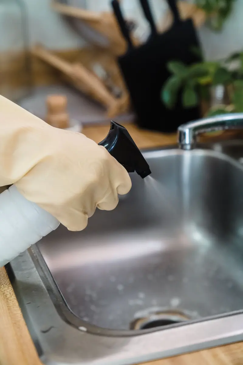 Spüle wird mit Handschuhen und Sprühflasche gereinigt