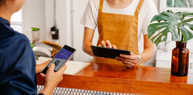 Mitarbeiterin bedient ein Smartphone an der Theke eines Cafés